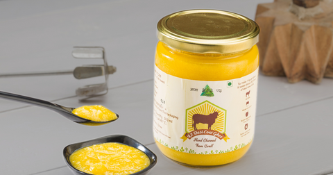 A glass jar of golden A2 Cow Ghee with a spoonful of ghee, highlighting its rich texture and purity.