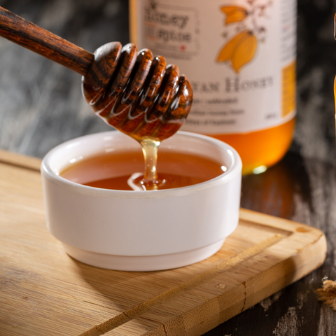 Honey dipper dripping golden honey into a bowl on a wooden board, with a honey jar in the background.