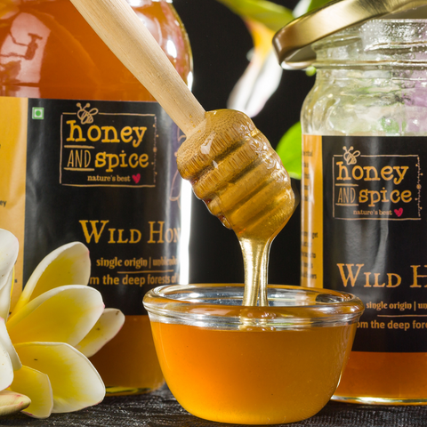 Wooden honey dipper drizzling honey into a glass bowl, surrounded by Wild Honey jars.