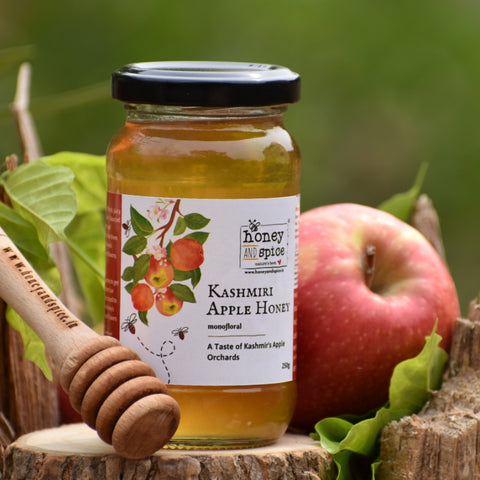 Kashmiri Apple Honey jar with wooden dipper, fresh apple, and green leaves.