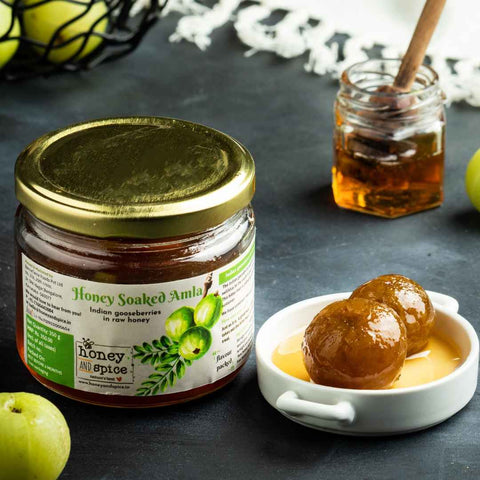 Honey Soaked Amla served with fresh gooseberries placed on table surface with honey jar.
