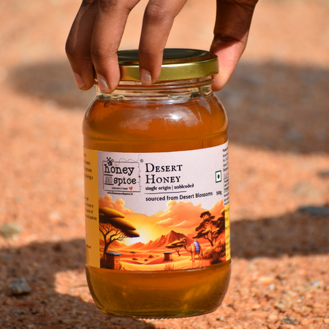 Hand holding Pure Desert Honey jar – placed on desert sand.