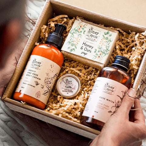 Hand holding gift box with skincare products including body cream, body wash, and lip balm