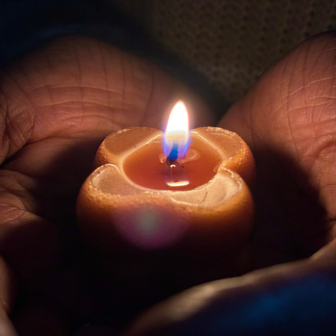 Beeswax candle in a floral shape glowing warmly in hands.
