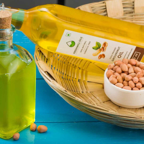 Groundnut Oil bottle in a basket with raw peanuts and a small bowl of oil.