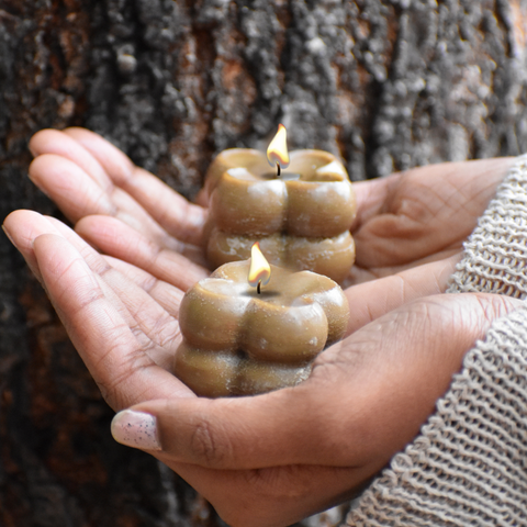 Beeswax candles in hands, showcasing a sustainable and natural design with a tree bark backdrop.