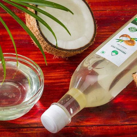 Coconut Oil bottle on a red table, styled with fresh coconut halves and a glass bowl.