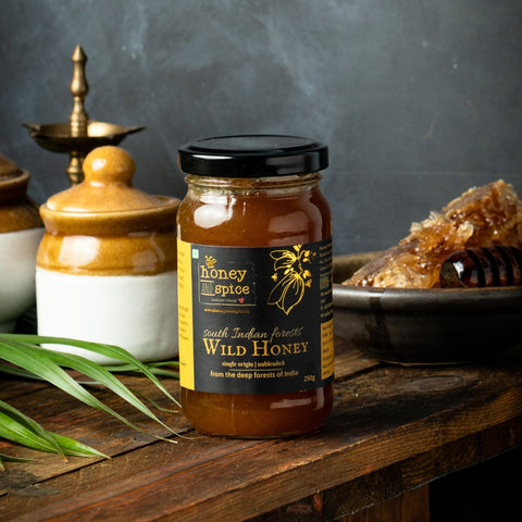 South Indian Forests Wild Honey jar of 250g placed beside honeycomb and kitchen props on a rustic table.