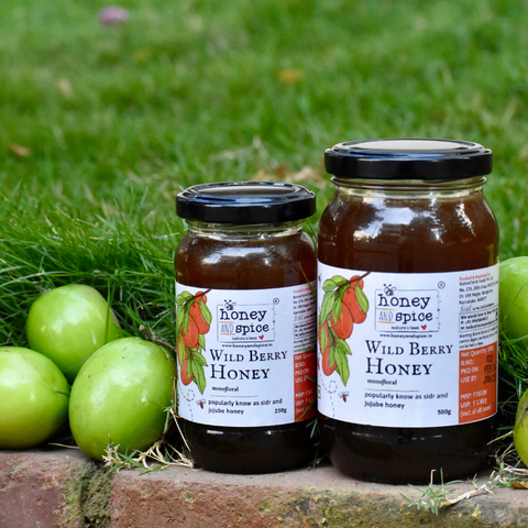 Two jars of Wild Berry Honey 250g & 500g. placed on a grassy surface with green Berry in the grass background.
